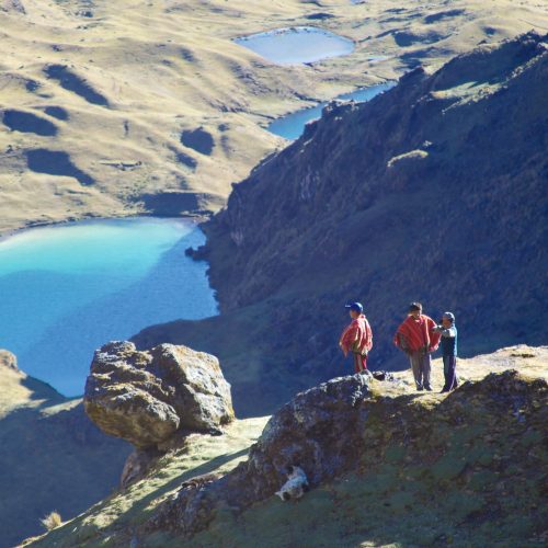 Rural shepherd boys, in their traditional red-woven ponchos, taking in the vista as they mind their grazing herd of alpaca & llama.